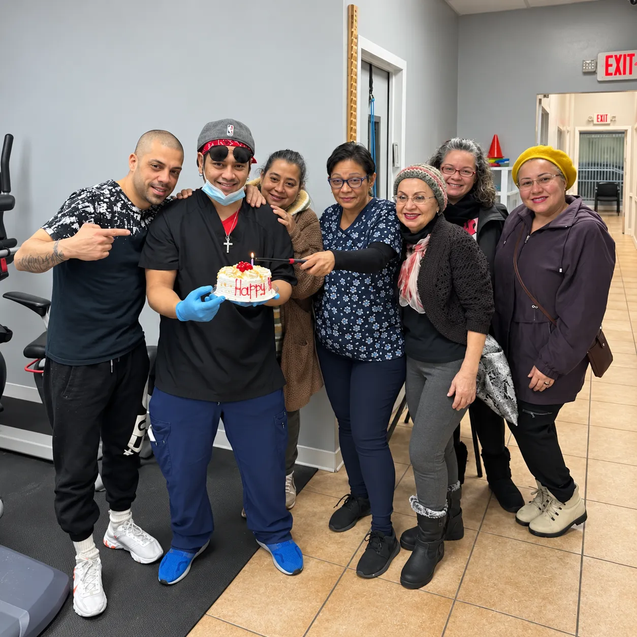 RedCore staff and patients gathered together in the clinic around a birthday cake, laughing.