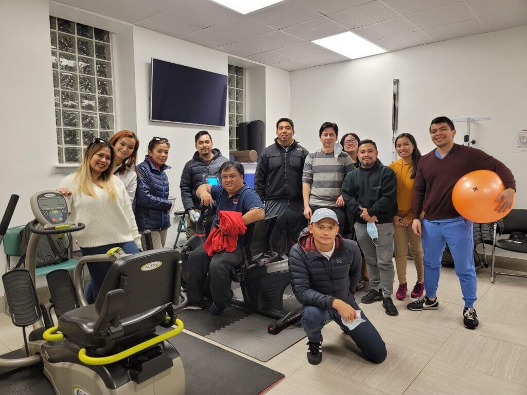 Group photo of RedCore Physical Therapy team with patients in a physical therapy clinic, featuring exercise equipment and a welcoming atmosphere.